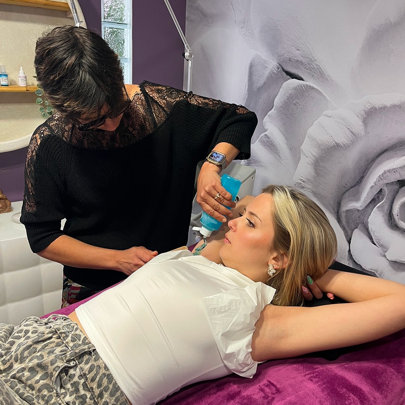 Esthéticienne appliquant un gel bleu sur le cou d'une cliente allongée pour un soin du visage ou du corps.