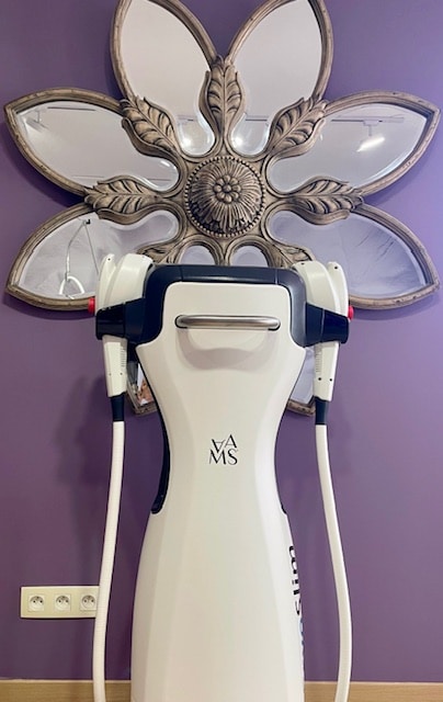 Machine VAMSlim : Esthétique et Amincissement Moderne Appareil de technologie esthétique VAMSlim blanc devant un mur violet et un miroir décoratif en forme de fleur.